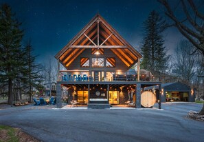 A large, two-story log cabin with a prominent gable roof, a covered front porch, and a large wooden barrel. - Pocono Family Retreat | Hot Tub, Sauna, Sleeps 14 (Blakeslee)