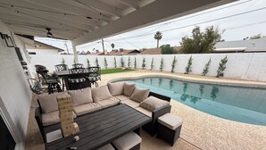 Un patio al aire libre con piscina, una mesa de madera oscura y un sofá color crema.