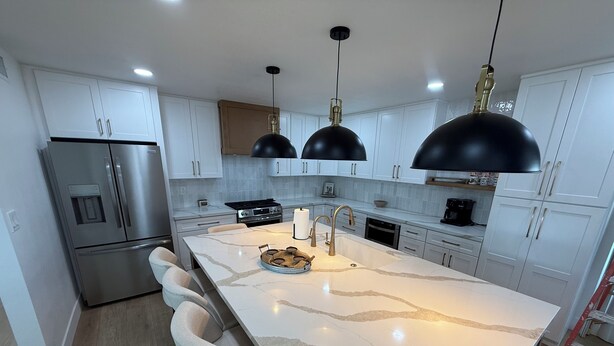 Una cocina moderna con armarios blancos, una isla grande con encimera de mármol, electrodomésticos de acero inoxidable e iluminación colgante.