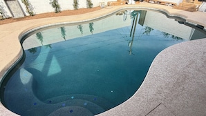 Una piscina con borde curvo y solárium con baldosas.