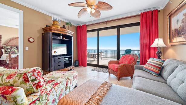 Sala de estar con sofá, sillón y televisor. Balcón con cortinas rojas y vistas al exterior.