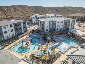 Um hotel moderno com várias piscinas, incluindo uma piscina central ampla e uma piscina menor com escorrega.