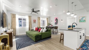 Ein modernes Wohnzimmer mit einem grünen Sofa, einem Essbereich und einer Kücheninsel.