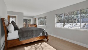 Ein geräumiges Schlafzimmer mit einem großen Bett, einer Holzkommode und mehreren Fenstern mit Blick auf eine verschneite Landschaft.