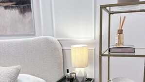 A modern living room with a grey sofa, a side table with a lamp and a bottle, and a gold-framed shelving unit with decorative items. - Cozy 1-bedroom studio in amazing Katowice, 24h check-in (Katowice)