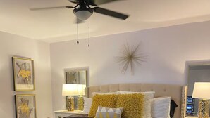 A bedroom with a bed, a ceiling fan, bedside tables, and a bench. - Spacious 4-bedroom house in beautiful Bartlesville with AC (Bartlesville)