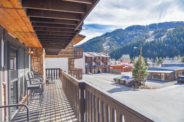 A balcony with a view of a mountainous landscape, a parking area, and a building with multiple windows and balconies.