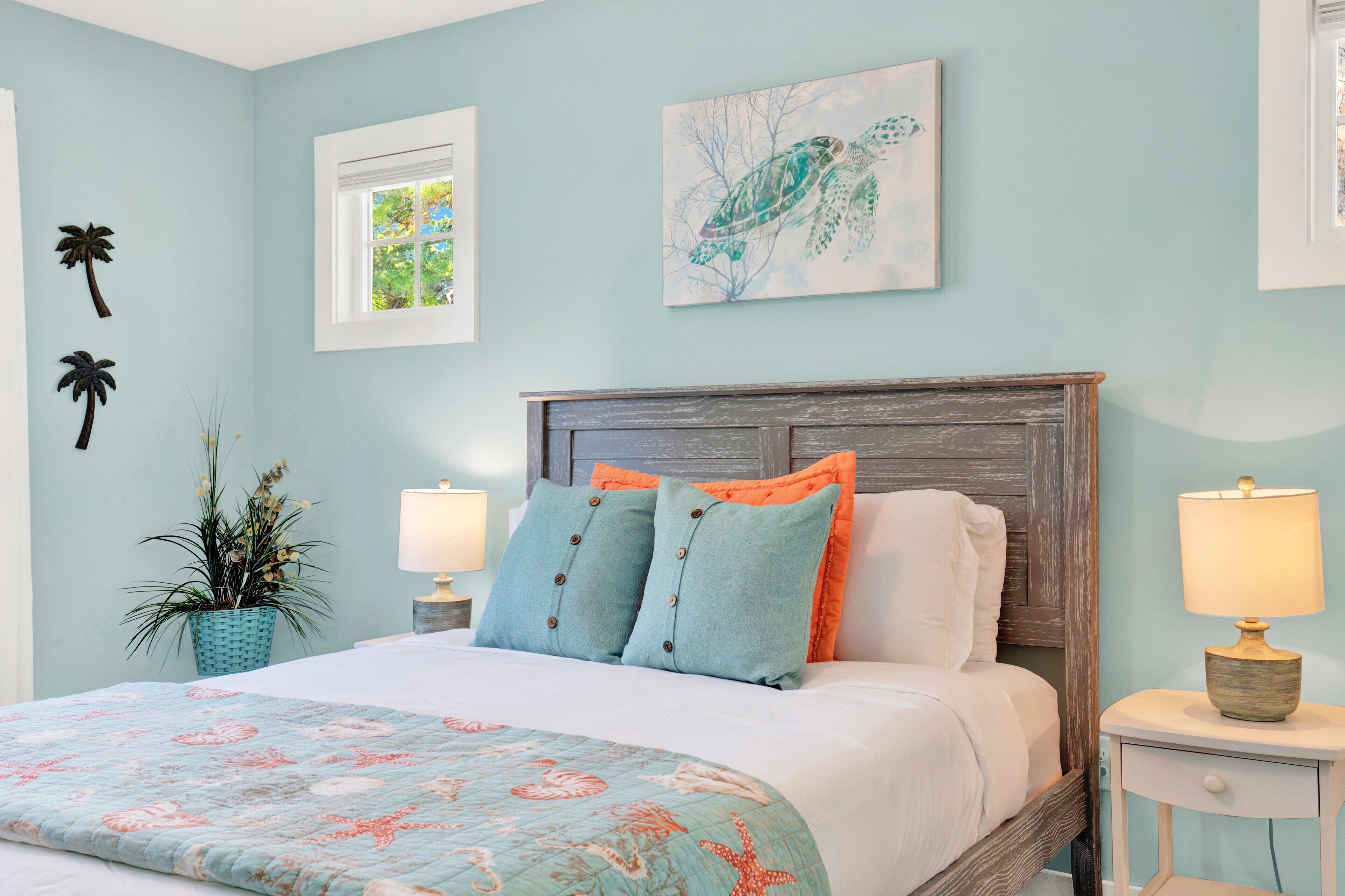A bedroom with a bed, two nightstands, a window, a plant, and wall art.