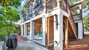 A two-story house with a covered patio, wooden deck, and a staircase leading to the upper level. - Unwind and Relax at Tybee Mist | Heated Pool Access (Tybee Island)
