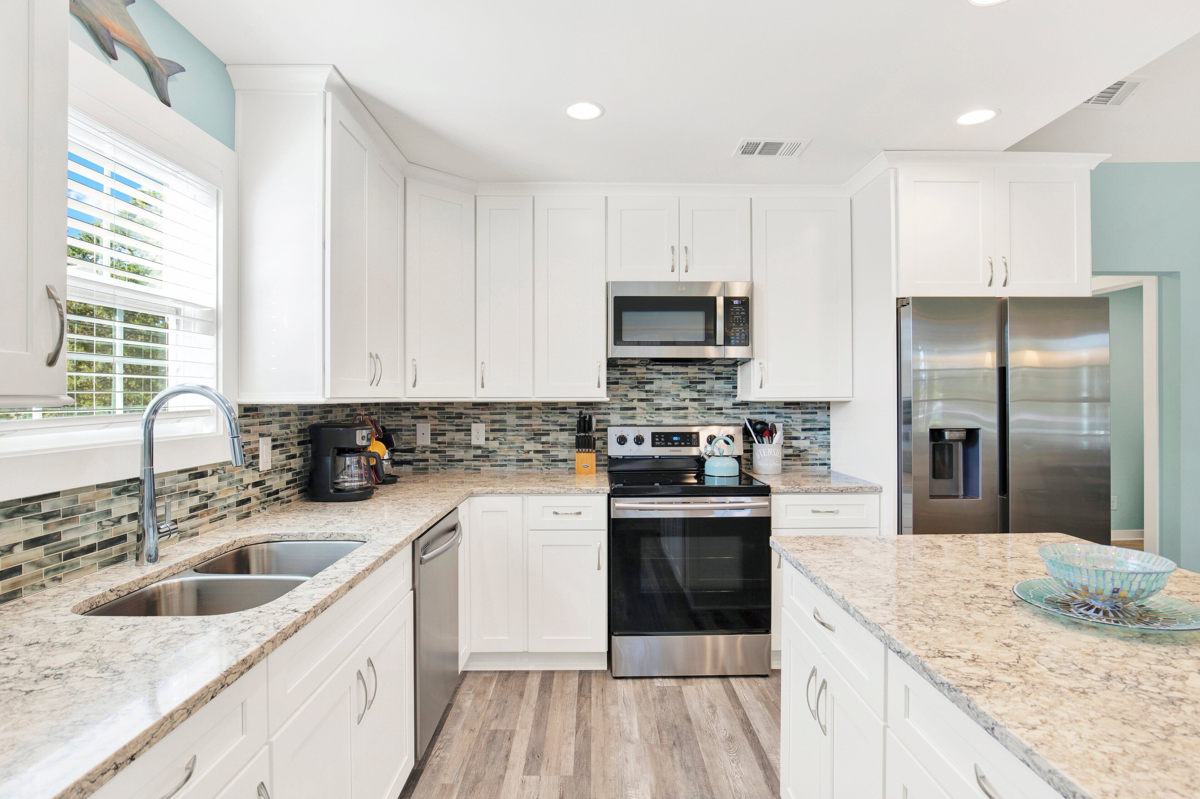 A modern kitchen with white cabinets, a stainless steel refrigerator, a microwave, and a built-in oven.