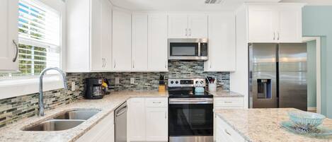 A modern kitchen with white cabinets, a stainless steel refrigerator, a microwave, and a built-in oven.