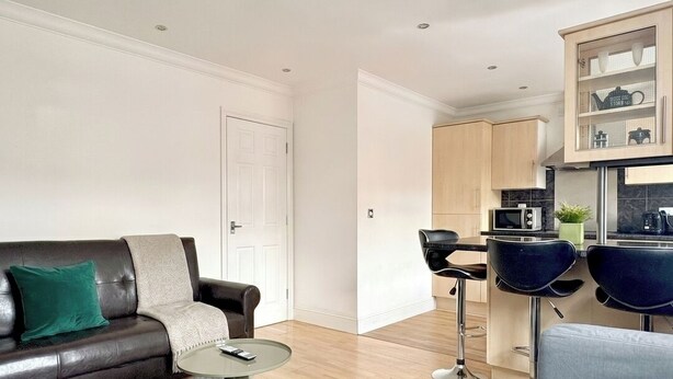 Un soggiorno moderno con divano, tavolino e angolo cottura con uno sgabello da bar.