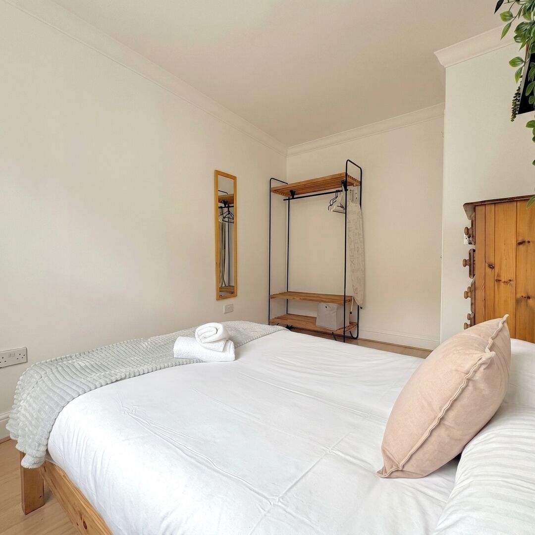 A bedroom with a bed, a wooden wardrobe, a mirror, and a hanging plant.