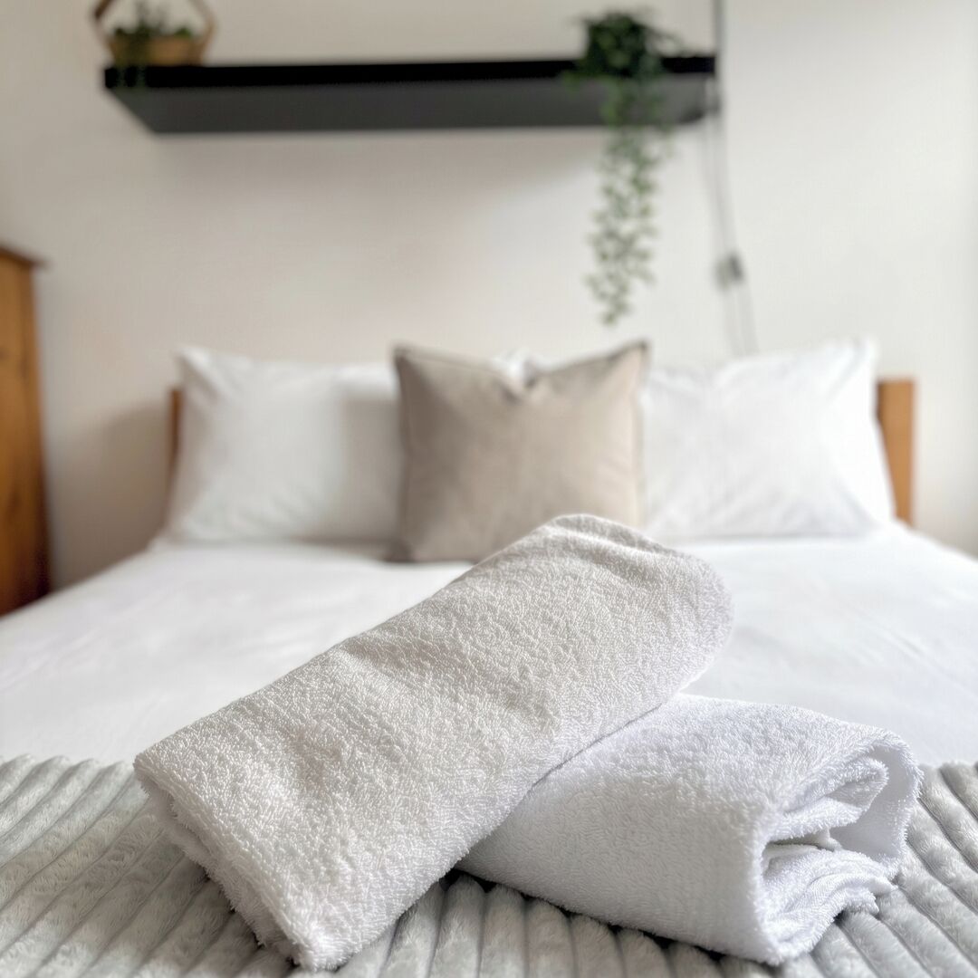 Una cama bien hecha con ropa blanca y una toalla blanca doblada encima.