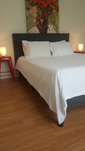 A neatly made bed with white linens, a dark headboard, and a wooden floor. There are two bedside tables with lamps, and a painting of flowers on the wall. - Cozy 1 bedroom house on quiet alley but close to town and mountain (Buena Vista)