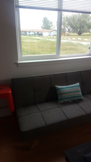 A room with a grey sofa, a window with blinds, and a red stool. - Cozy 1 bedroom house on quiet alley but close to town and mountain (Buena Vista)