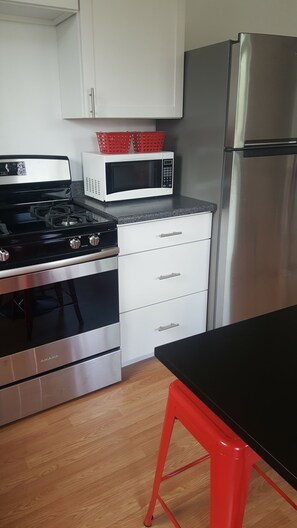 A kitchen with a stove, microwave, refrigerator, and a red chair. - Cozy 1 bedroom house on quiet alley but close to town and mountain (Buena Vista)