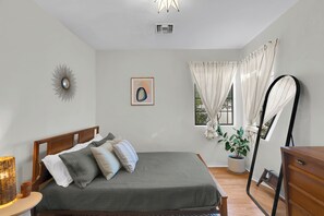 Une chambre à coucher avec un lit, une table de chevet, une lampe, une fenêtre avec des rideaux et une plante en pot.