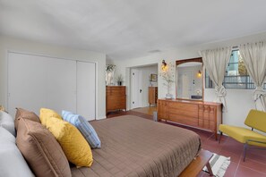 Ein Schlafzimmer mit einem großen Bett, einer hölzernen Kommode, einem Spiegel und einem gelben Sessel.