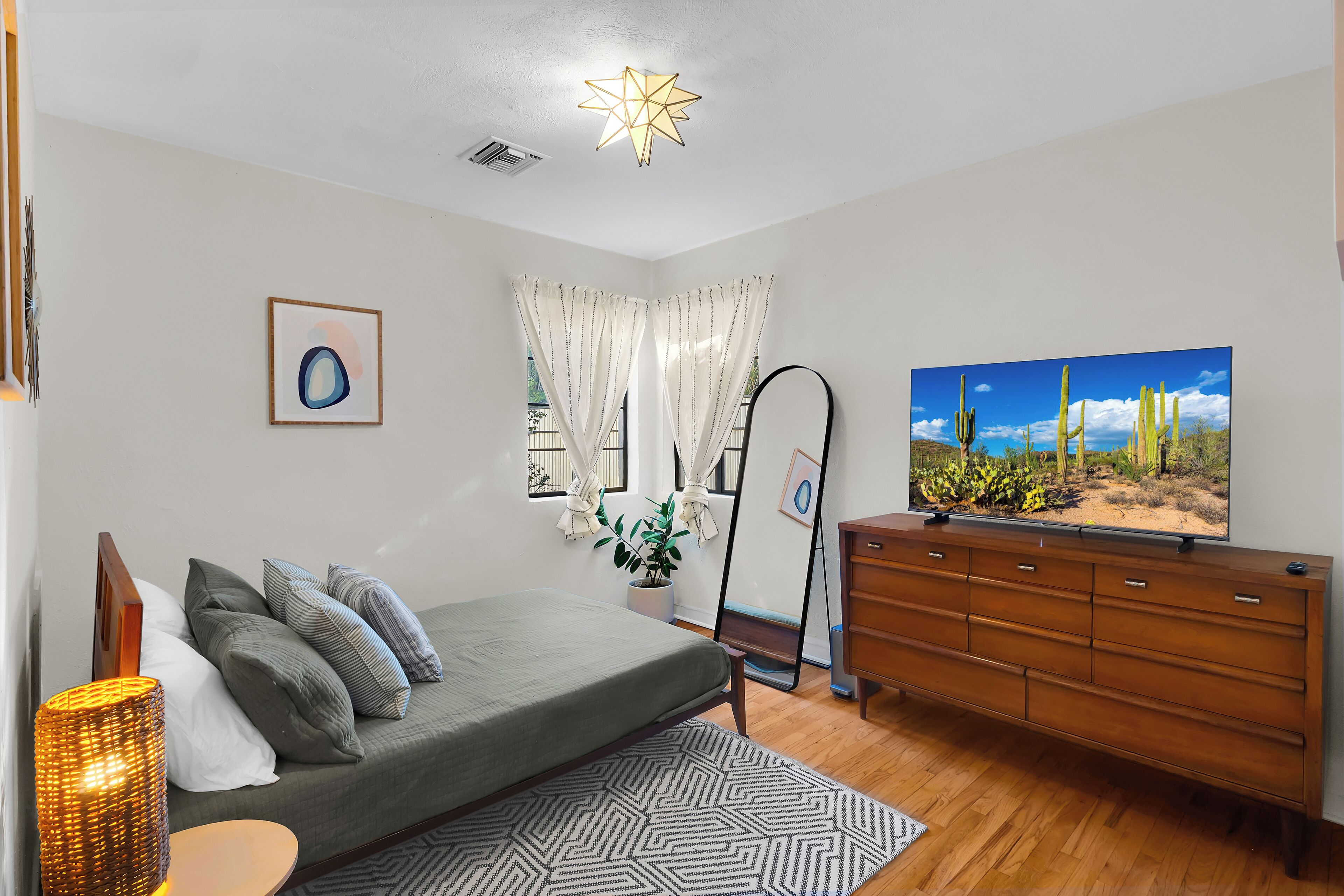 Une chambre à coucher comprenant un lit, une commode, un téléviseur, un luminaire au plafond en forme d’étoile et une fenêtre avec des rideaux.