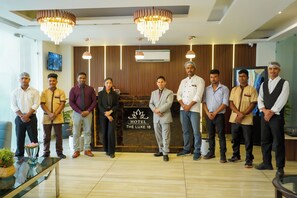 A group of people standing in a hotel lobby with a modern chandelier, a reception desk, and a sign that reads "Hotel The Luxe 18". - HOTEL THE LUXE 18 (Gurugram)