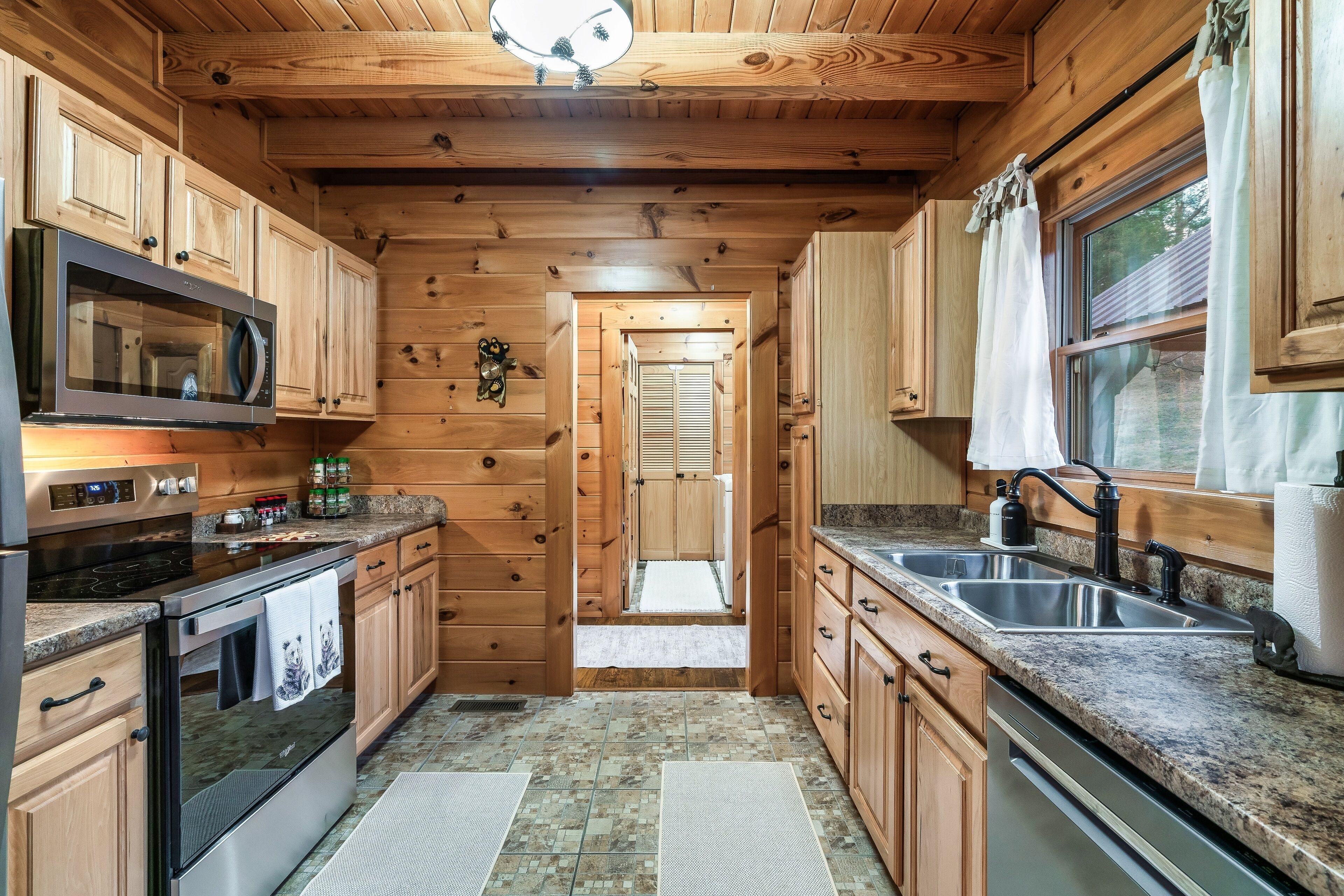 A wooden cabin kitchen with a microwave, stove, sink, and cabinets.