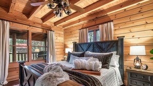 Quarto de cabana de madeira com uma cama grande, um banco de madeira e uma mesa de cabeceira com uma luminária.