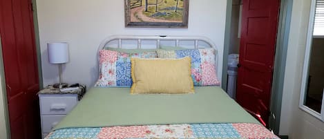 A small, neatly arranged bedroom with a single bed, a bedside table with a lamp, and a painting on the wall.