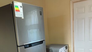 Een kleine keuken met een roestvrijstalen koelkast, een wasmachine en een witte deur.