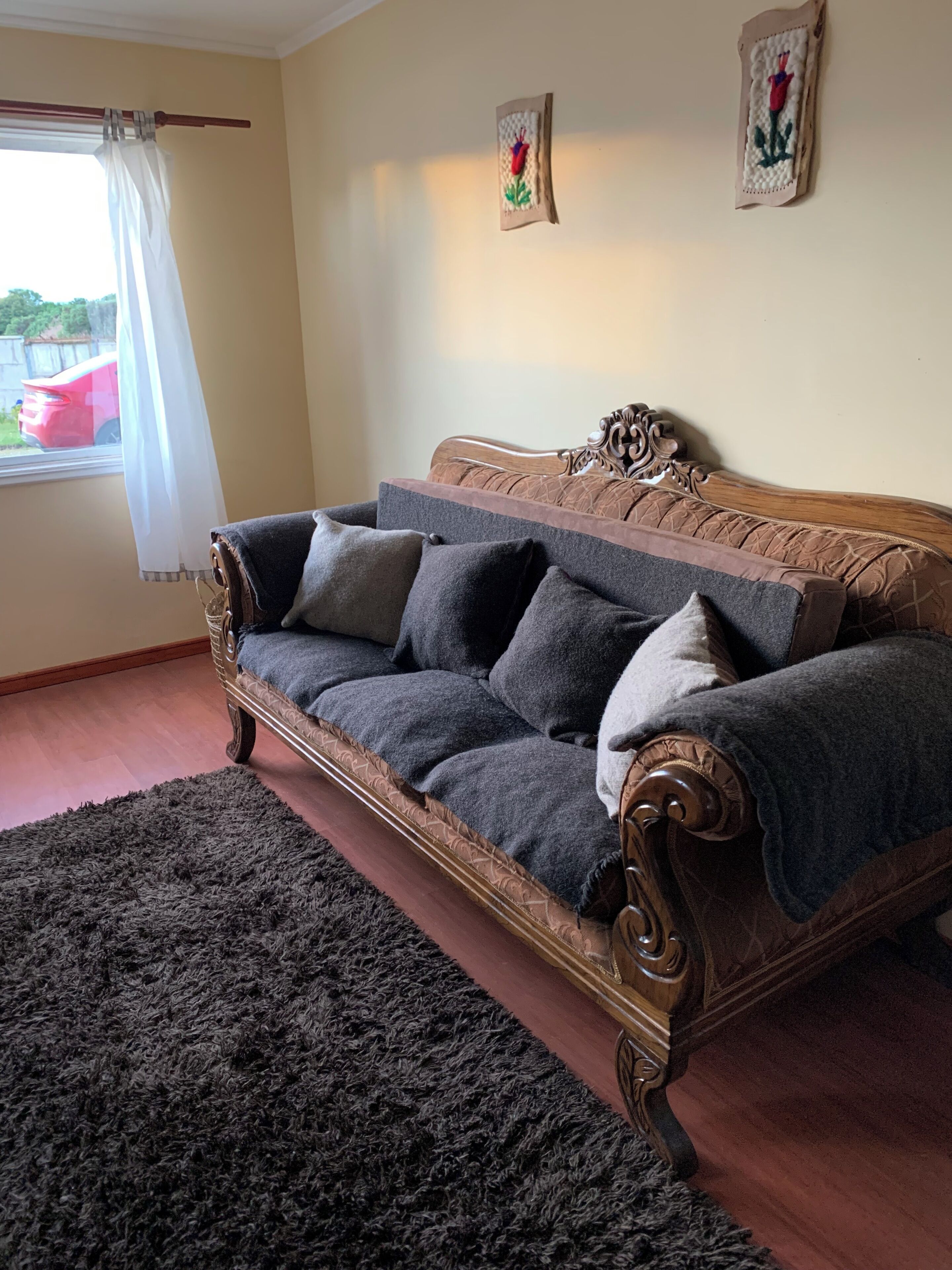 A cozy room with a vintage-style sofa, a dark shaggy rug, and a window with a white curtain.