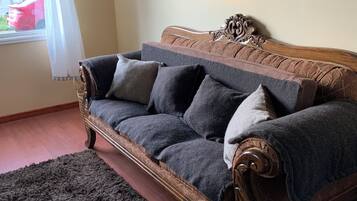 A cozy room with a vintage-style sofa, a dark shaggy rug, and a window with a white curtain.