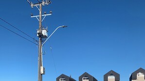 Een omheind woongebied met huizen, een lantaarnpaal en een betonnen paal.