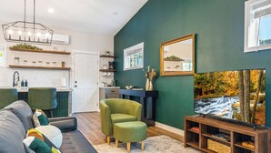 A modern living room with a dark green wall, a large flat-screen TV, a grey sofa, a green armchair, and a wooden entertainment unit. - The Evergreen Escape - Spacious 1 bed Unit (Kennewick)