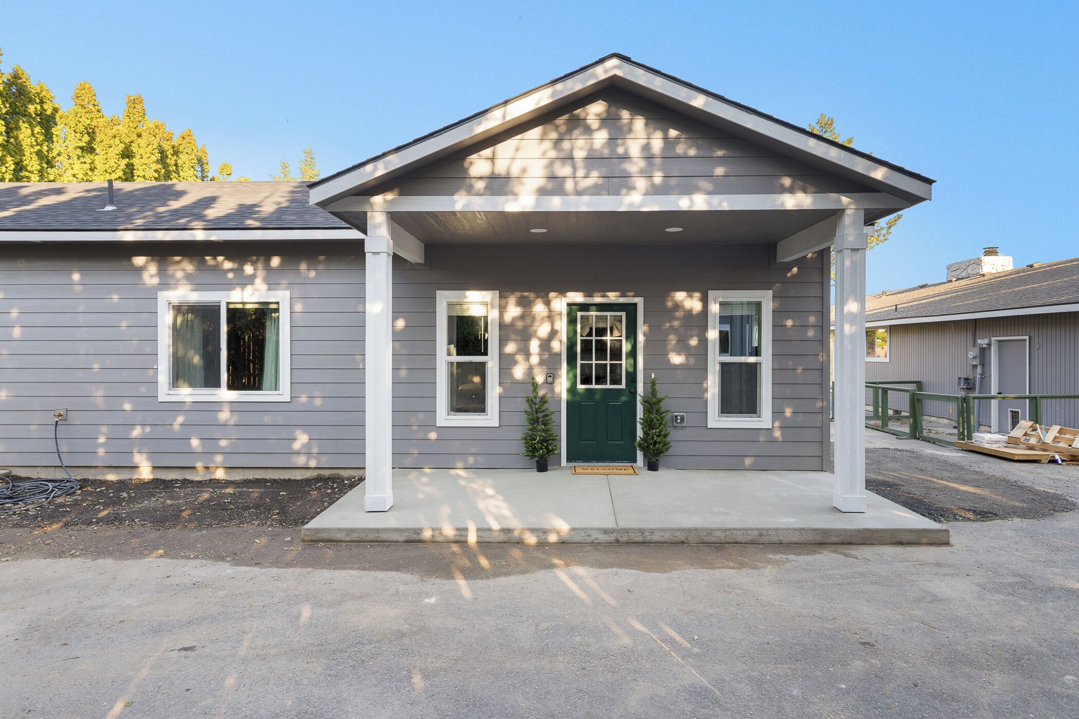 A two-story house with a front porch, a green door, and two small potted plants.