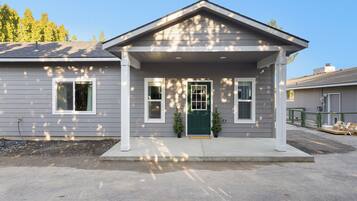 A two-story house with a front porch, a green door, and two small potted plants.