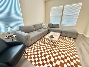 Ein modernes Wohnzimmer mit einem grauen Ecksofa, einem runden Couchtisch und einem Schachbrettmuster-Teppich.