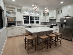 A modern kitchen with white cabinetry, a large island with bar stools, stainless steel appliances, and a chandelier.