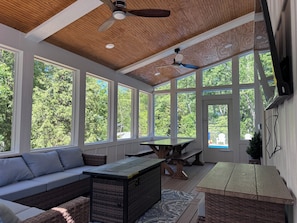 A sunroom with large windows, a ceiling fan, a table, and a sofa.