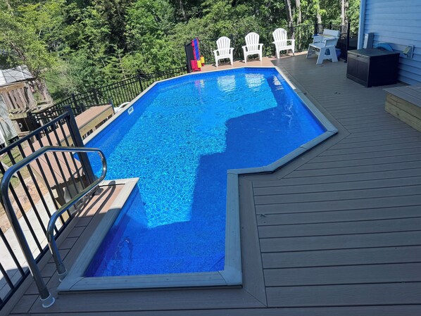 A swimming pool with a wooden deck, surrounded by a black metal fence, and white Adirondack chairs. - Amazing Lake views, semi private beach, private heated pool, hot tub & game room (South Haven)