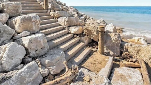 Een stenen trap die naar een strand leidt, onder heldere luchten.