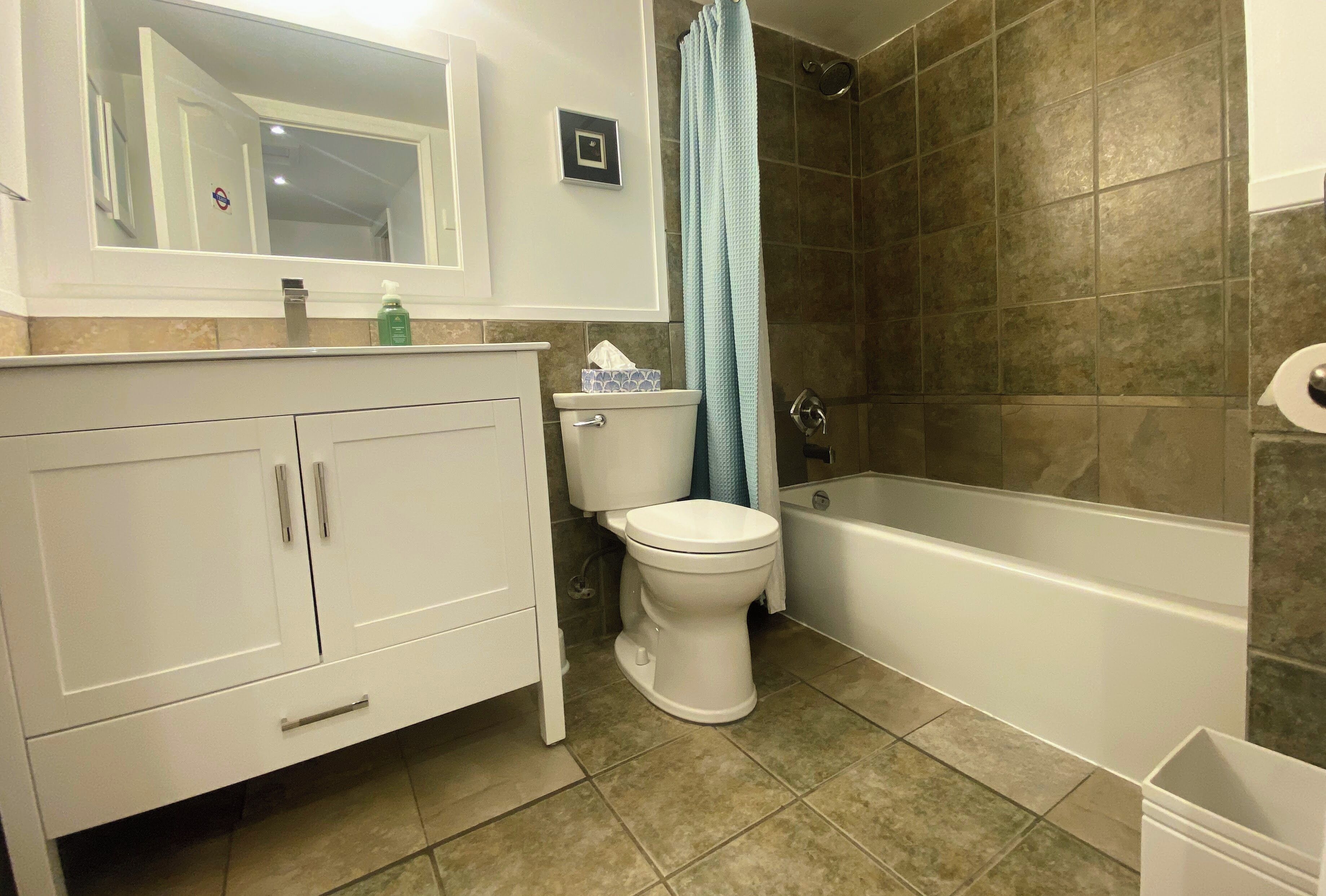 Une salle de bain avec des toilettes blanches, une baignoire et un espace douche aux carreaux bruns.