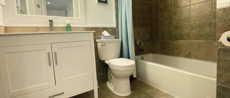 Une salle de bain avec des toilettes blanches, une baignoire et un espace douche aux carreaux bruns.