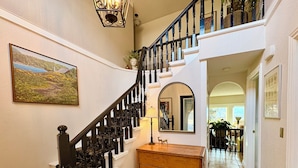 A grand staircase with ornate black balusters, a wooden bench, and a mirror reflecting the interior. - The Susie Pearl Bed & Breakfast (Kelowna)