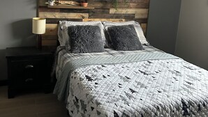 Un dormitorio con cama, mesita de noche, estante en la pared con plantas y ventilador de techo.