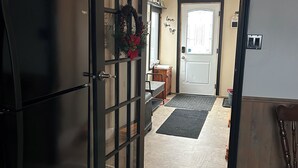 Una cocina con un refrigerador negro, una puerta con panel de vidrio y un pasillo que lleva a un comedor.