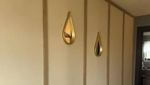 Un pasillo con paredes color beige y piso de madera. Se observan dos adornos dorados en la pared y una señal blanca sobre un estante negro.