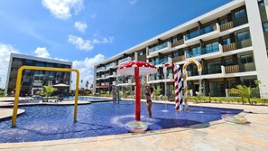 A swimming pool area with a water play structure, a large building with balconies, and a clear sky. - Mana Beach Experience By Aft (Ipojuca)