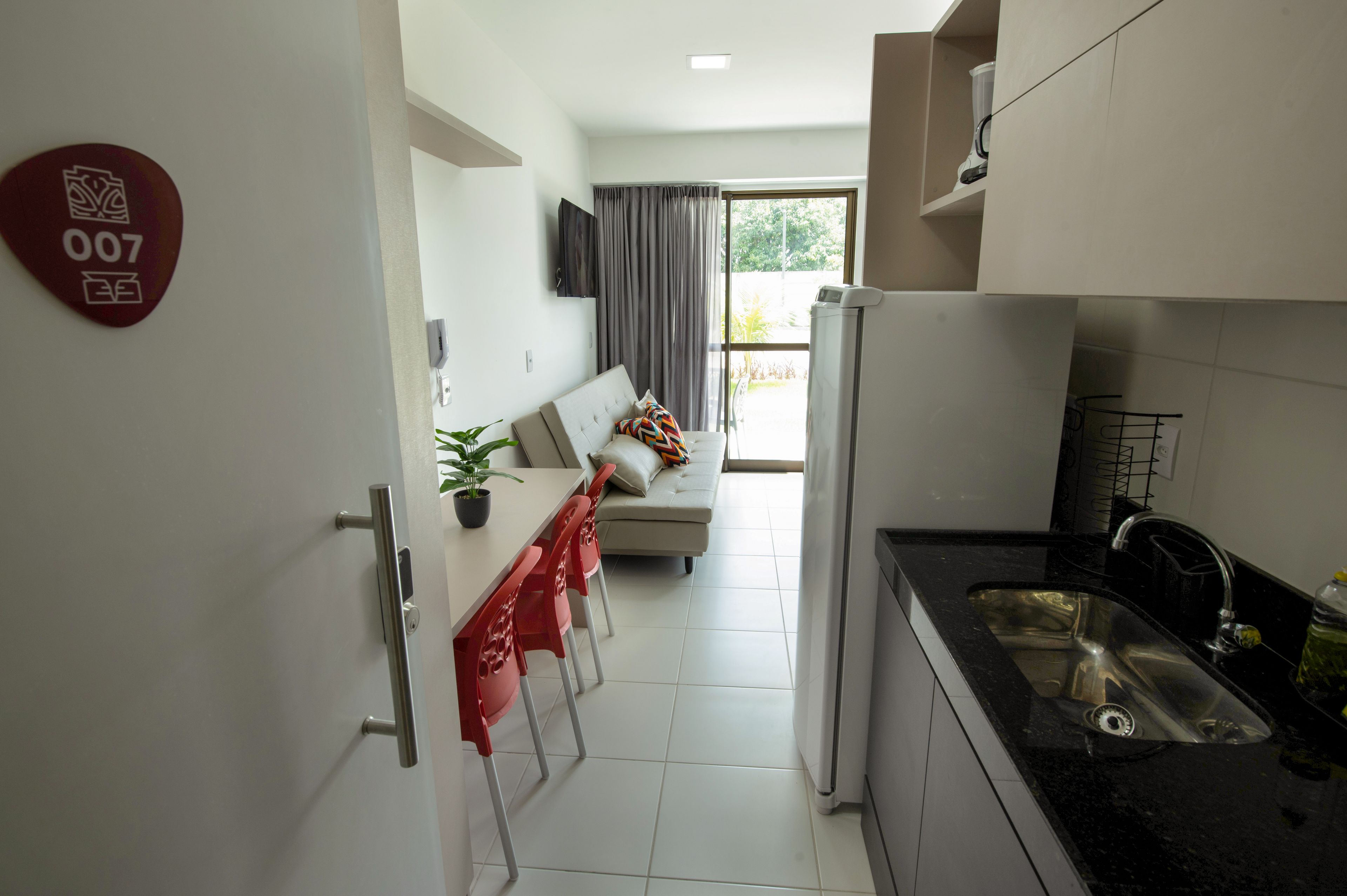 A modern kitchen with a dining area, a sofa, and a large window.