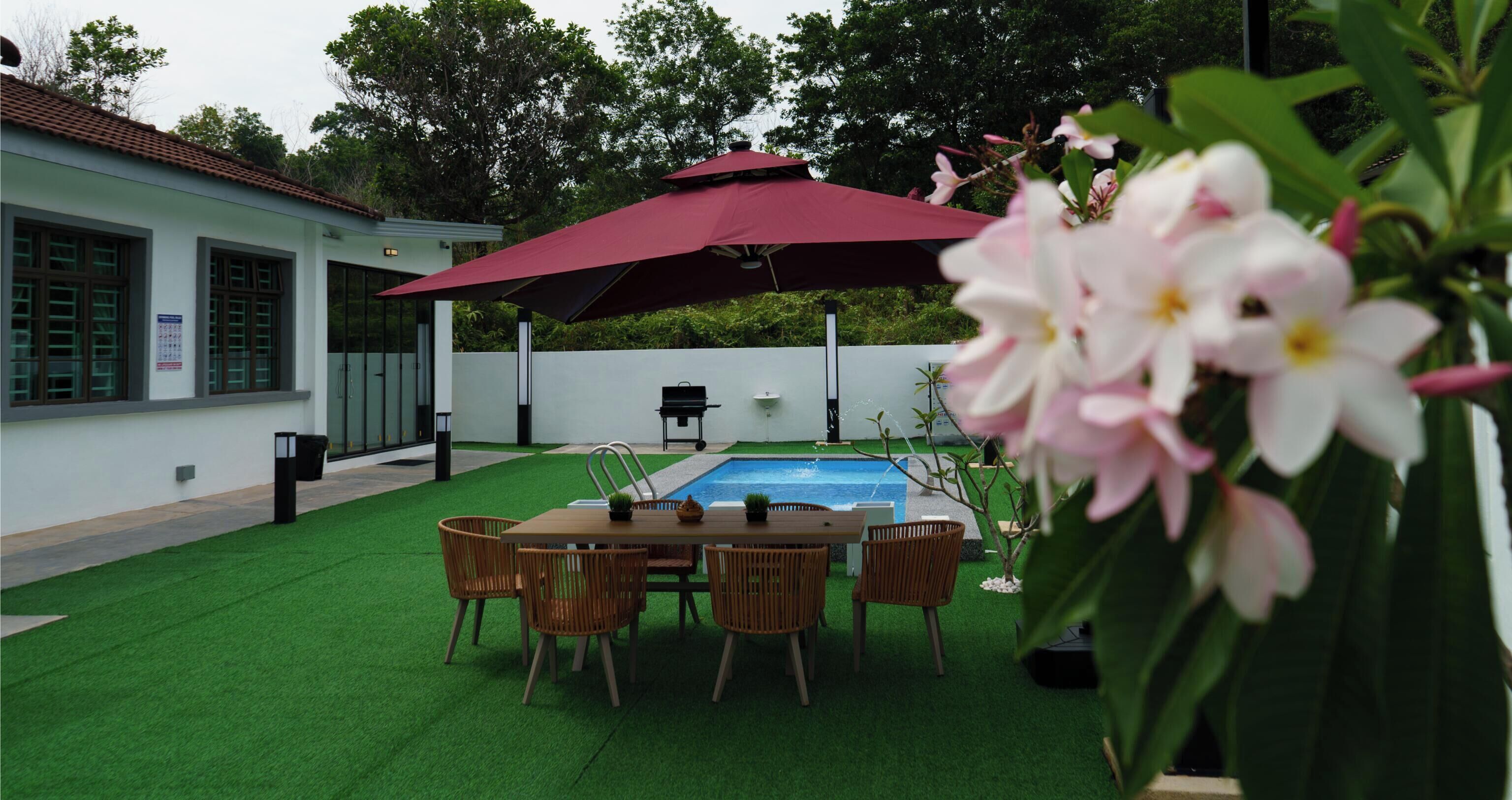 A pool area with a table and chairs, surrounded by a white fence and greenery.