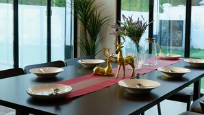 Ruokailutilassa on pitkä pöytä, jonka ääreen on katettu kuudelle, ja pöydän ympärillä on tuoleja. Pöydällä on koriste-esineitä, kuten maljakko kukkineen ja kultainen peuranpatsas.